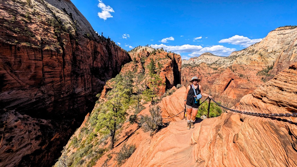 Hiker on the narrow sandstone ridge holding the safety chain, Zion Canyon behind