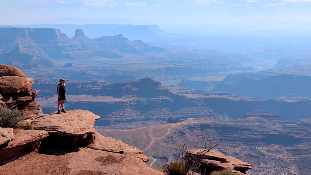 Hiker on a sandstone ledge overlooking the vast canyon at Dead Horse Point State Park, Utah