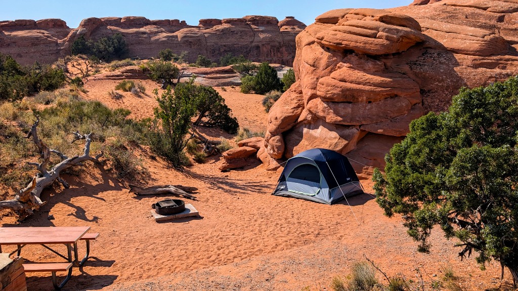 Dome tent, picnic table, and fire ring on red sand beside sandstone fins, Devils Garden Campground, Arches National Park