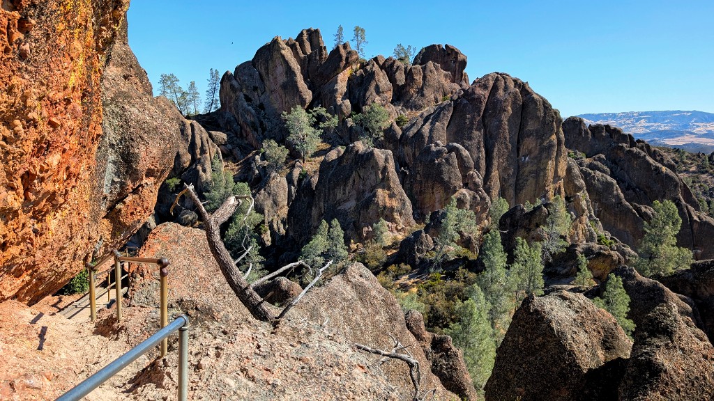 High Peaks trail at Pinnacles National Park – volcanic rock spires, a dirt path with metal handrails along a cliff edge, and pine trees in the valley below
