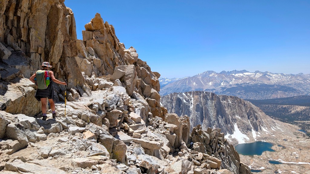 Hiker on the Mount Whitney trail near the summit with the Sierra Nevada stretching into the distance and an alpine lake below