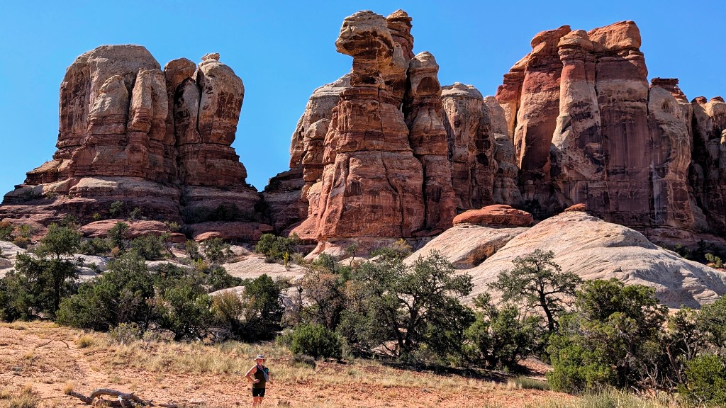 Hiker dwarfed by towering red and white sandstone spires at Chesler Park in the Needles district of Canyonlands National Park